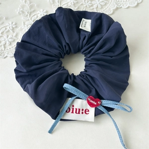 Detail of navy scrunchie featuring a denim bow, white label, and red heart pendant