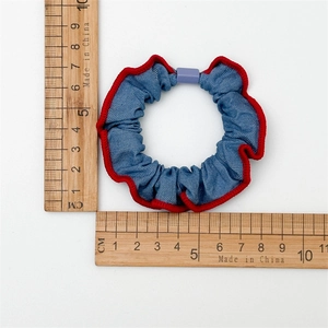 Haargummis aus Denim mit roten Ziernähten auf Messlinealen für die Größenangabe