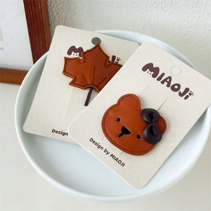 Detail view of brown maple leaf and bear leather hair clips with stitching on display card