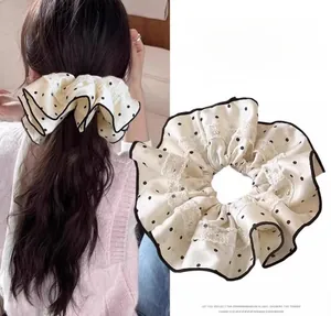 Detail of cream satin scrunchie with black polka dots and delicate lace edging