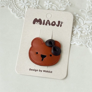 Detail of cute brown leather bear hair clip with bow on white lace background
