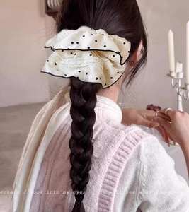 Detailed view of a large beige satin scrunchie with black dots and white lace trim