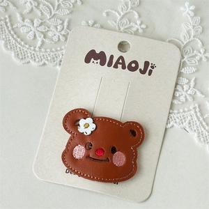 Close-up of a brown leather teddy bear hair clip with embroidery on a lace background