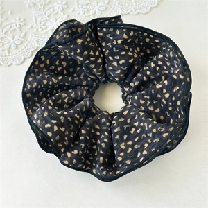 Close-up of black satin scrunchie with golden heart pattern on off-white background