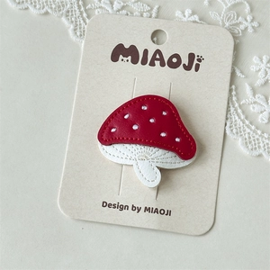 Close-up of red leather mushroom hair clip with detailed embroidery and stitching on card