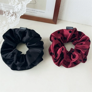 Close-up of premium satin scrunchies in black and burgundy polka dot with fashion label
