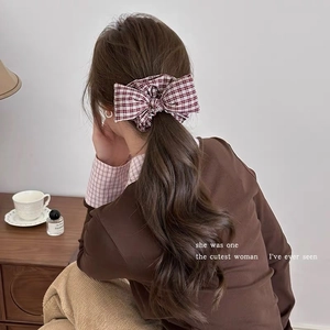 Detail view of a vintage red plaid bow scrunchie styled on a low ponytail hair tie