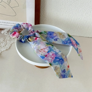 Detail of floral watercolor print hair scrunchie with long ribbon on a white plate