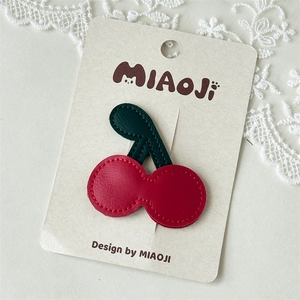 Detail of red leather cherry hair clip with green leaves and neat stitching design