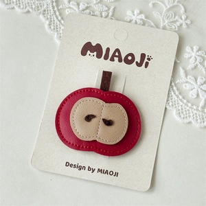 Detailed close-up of a red leather apple hair clip with fine stitching on a lace display