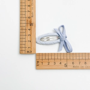 Dettaglio del fermaglio per capelli con fiocco azzurro e righello per le dimensioni