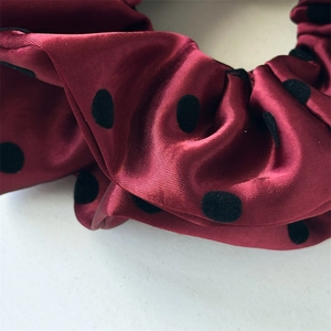 Detailed view of dark red satin scrunchie featuring elegant black flocked polka dots texture