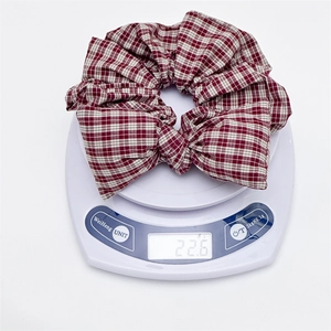 Detail showing red and white plaid bow hair scrunchie weighing 22.6g on a digital scale