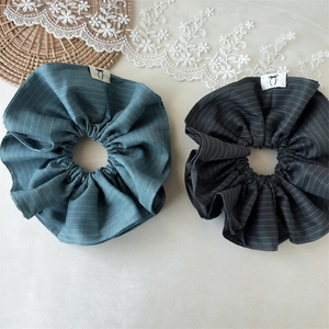 Close-up of two striped fabric scrunchies in grey and blue on a lace aesthetic background