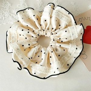 Close-up of cream satin scrunchie with black dots, lace details and ruffled edges