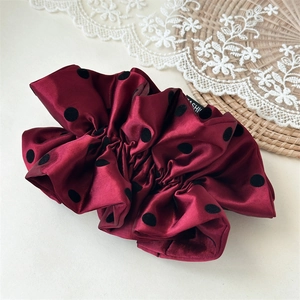Close-up of a burgundy satin polka dot scrunchie featuring a fashion label on lace background