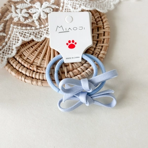 Dettaglio di due elastici per capelli con fiocco celeste per bambina su cartoncino