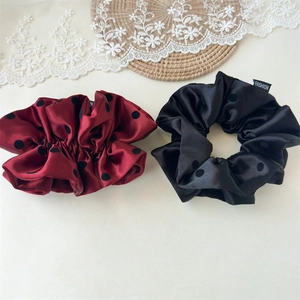Close-up of premium satin polka dot scrunchies on a decorative woven mat background