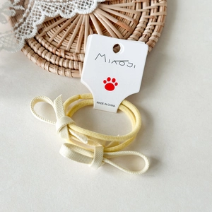 Dettaglio di un paio di elastici per capelli con fiocco giallo su cartoncino bianco