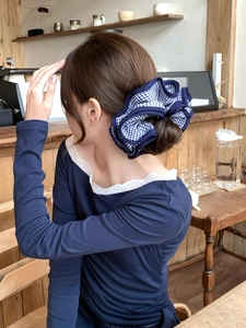 Dettaglio di elastico oversize a scacchi blu su uno chignon basso in ambiente naturale