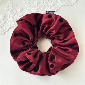 Detailed close-up of burgundy satin scrunchie with black polka dots and fashion label