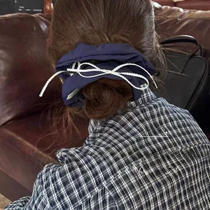 Detail view of navy blue silk scrunchie with white pearl bow and branded logo tag