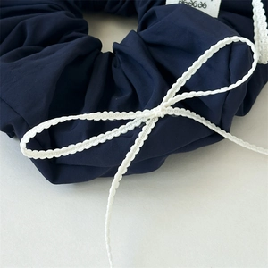 Close-up of navy blue scrunchie with white wave-edged bow and brand label detail