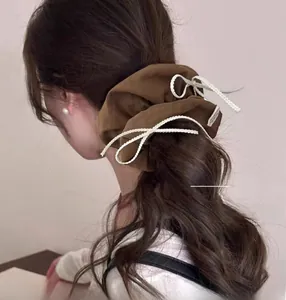 Detailed view of a brown fabric scrunchie with white woven cord on a ponytail