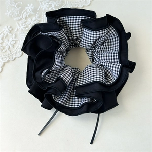 Detail eines großen schwarzen Gingham-Haargummis mit langen Bändern auf weißem Hintergrund