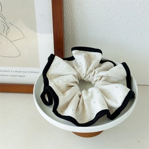 Détail d'un chouchou en tissu crème à carreaux avec bord noir et strass étincelants