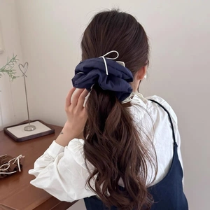 Detail of a navy blue bow scrunchie with white ribbon on a ponytail hairstyle