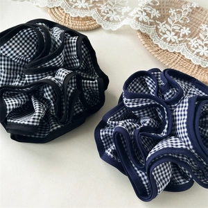 Dettaglio di elastici scrunchie a scacchi neri e blu su sfondo beige