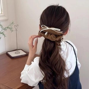Close-up of deep brown scrunchie with white woven bow detail worn on model's hair