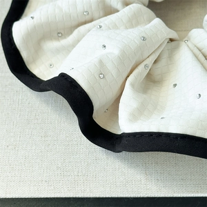Détail macro du chouchou matelassé blanc avec strass argentés et bordure en tissu noir
