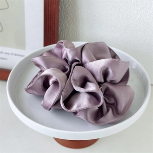 Detail of purple satin scrunchie with silky folds displayed on white ceramic tray