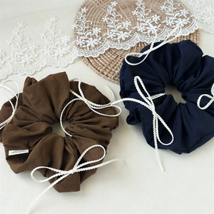 Close-up of brown and navy scrunchies with white lace bows on a woven coaster