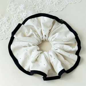 Détail d'un chouchou en tissu gaufré blanc orné de strass et d'une étiquette faite à la main