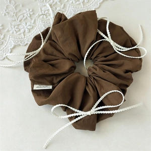 Close-up of deep brown scrunchie with lace bows and brand tag on creamy surface