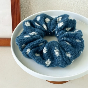 Detailed close-up of a dark blue knitted scrunchie with white polka dots on a tray