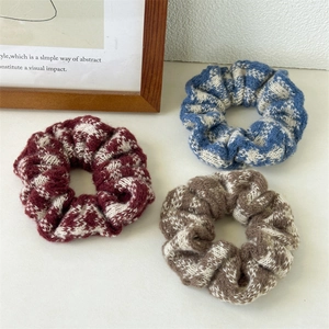 Close-up of three knitted checkered scrunchies in burgundy, blue, and coffee brown colors