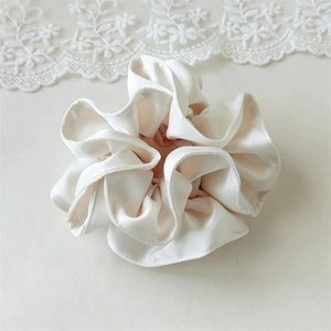 Macro detail of glossy white satin scrunchie showing pleated texture and silky fabric