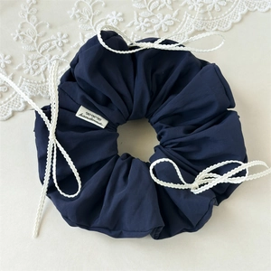 Close-up of a blue matte scrunchie with white woven bows and a handmade textile label