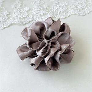 Close-up of a large satin scrunchie in mauve gray with pleated fabric and pearl luster