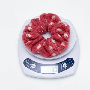 Detail shot of a red knitted polka dot hair scrunchie weighing 13.0g on a scale