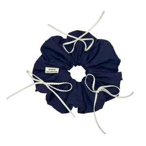 Navy blue fabric scrunchie with white lace bows and a handmade label on white background
