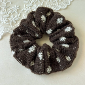 Detail of dark brown knitted scrunchie with white heart patterns and soft wool texture