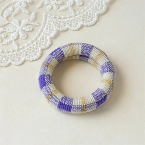Detail of purple and beige checkered fabric scrunchie with soft woven texture on white lace