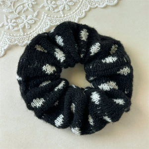 Detail of black knitted scrunchie with white polka dots showing soft yarn texture