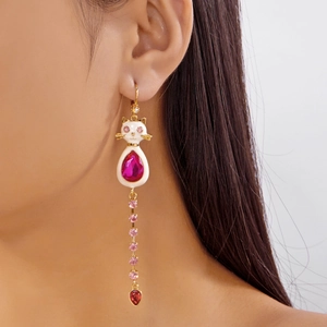 Vue détaillée de la boucle d'oreille chat asymétrique avec gemmes roses et pompons dorés