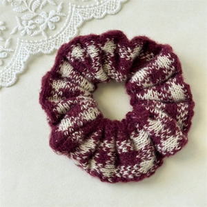 Close-up of a burgundy and beige plaid knit hair scrunchie on a lace background